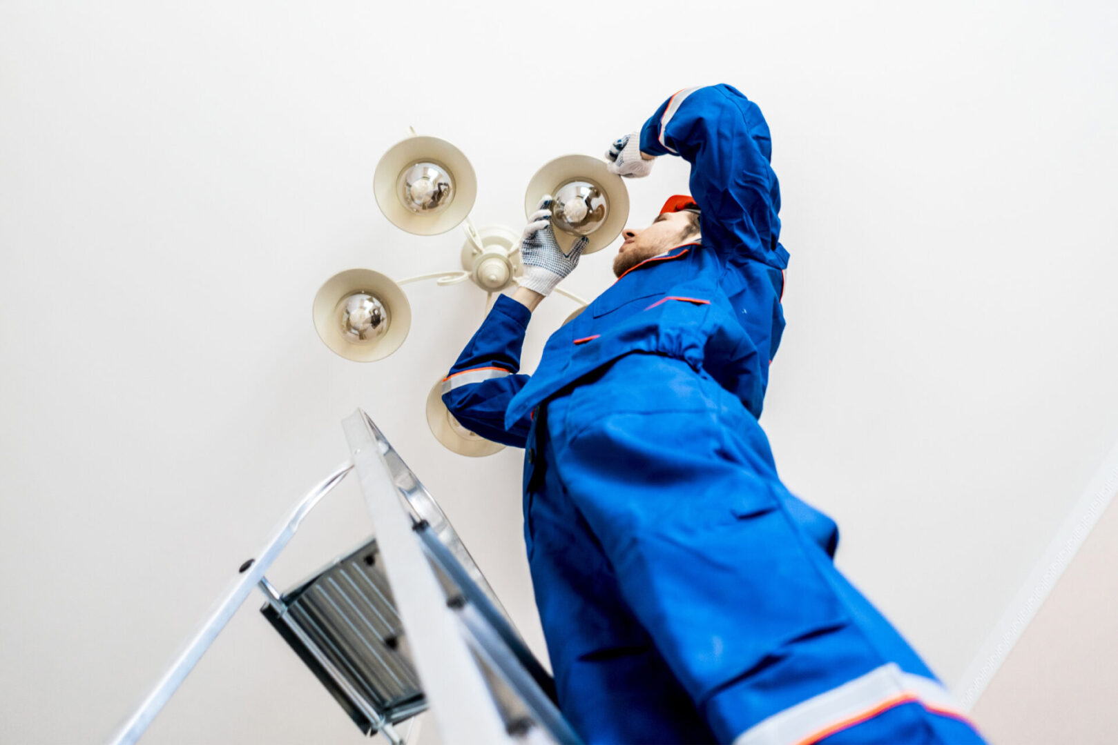 worker in uniform standing on the ladder and repair the chandelier at home