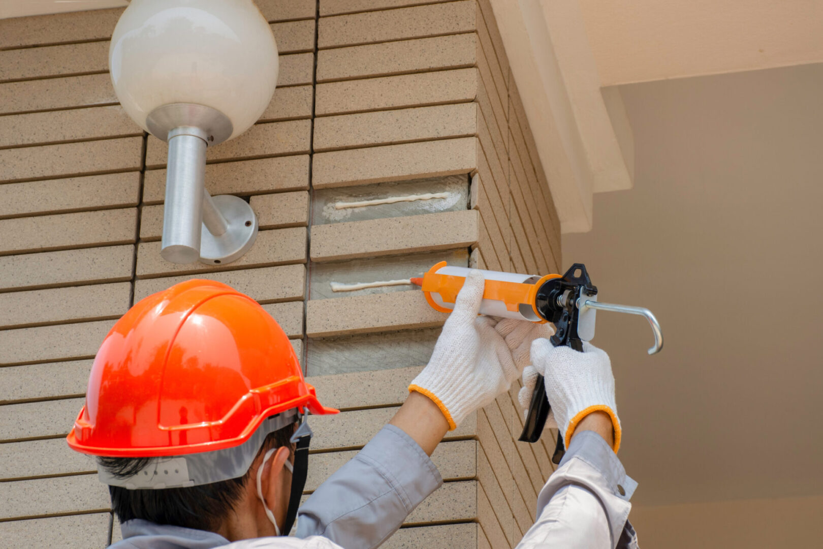 Worker man hand holding and using glue gun ( silicone tube or manual caulking gun ) with polyurethane or sealant to fix the sandstone tile . Maintenance construction concept.